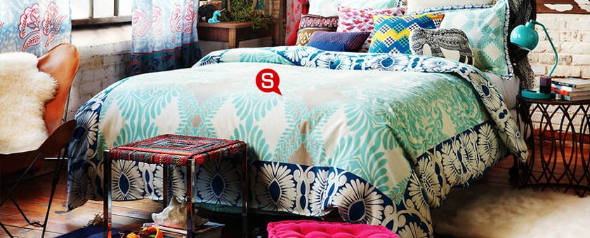 Urokliwa sypialnia z łóżkiem ozdobionym kolorową pościelą. Drewniane elementy i pstrokate dekoracje tworzą idealne połączenie.